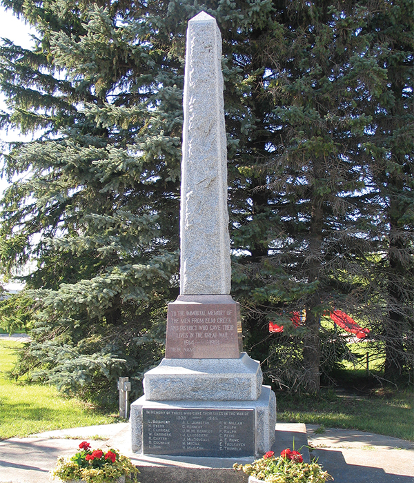 Memorial at Elm Creek. The red stone directly below the obelisk is engraved “To the immortal memory” of the sixteen men (their names on the sides of the stone) from the district who died in the Great War. Five battle sites are listed on the back. The lower, dark grey stone, tablet at the bottom was added later, and reads “In memory of those who gave their lives in the war of 1939–1945.” It lists 21 names.