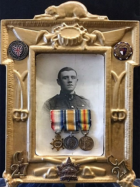 Framed picture of Private J. Denny taken in London circa 1915 with Canadian service cap badge, collar tabs and war service badges added post war