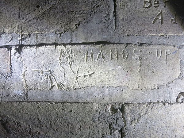 A man holding a pistol with the inscription “HANDS UP” inside one of the jail cells