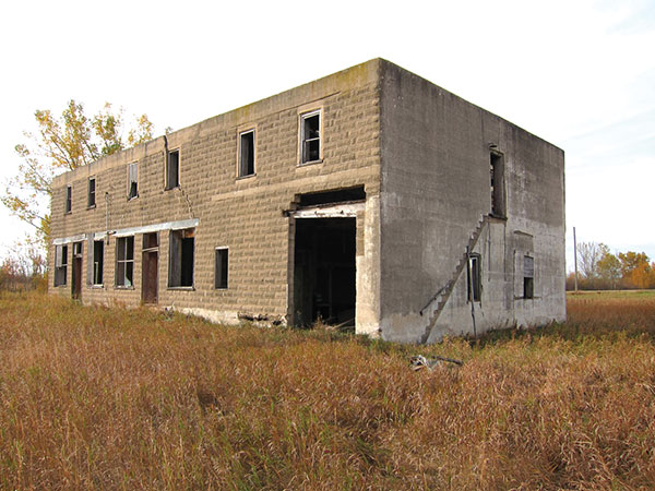 Kilkenny General Store (Broomhill, RM of Albert). This two-storey building was built for William Kilkenny and his brother John. In its heyday, the Kilkenny store was the centre of the community. A hand-operated gasoline pump sat at the south end, in front of an entrance to the store and post office, with an implement agency and garage at the north end. Rooms on the upper storey were used as residential space. The business was operated by a succession of Kilkennys until it closed in September 1964. The building&rsquo;s east and south walls are made from patterned concrete blocks. The roof is gone and the interior floors have failed in several places but, otherwise, the concrete structure is largely intact. Pressed metal wall and ceiling panels from the interior have been salvaged by a grandson of the last owner and are available for purchase.